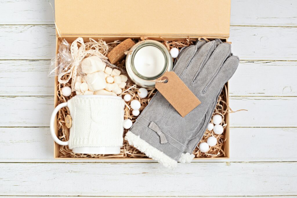 Preparing care package, seasonal gift box with mug, candle, warm gloves and christmas ornament